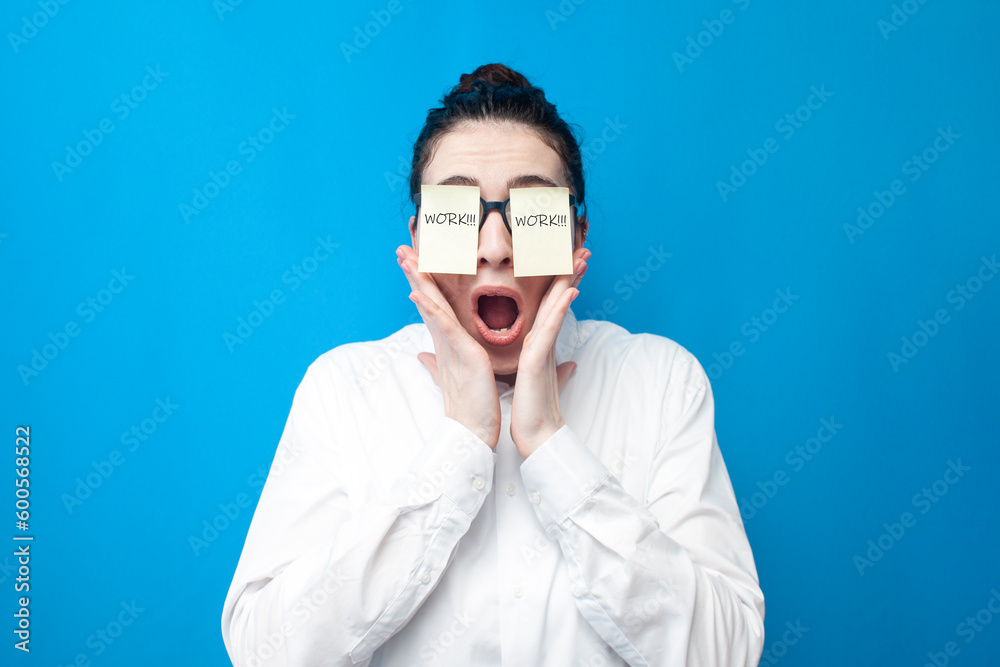 shocked woman manager screaming on blue background, girl office worker with papers in front of her eyes surprised
