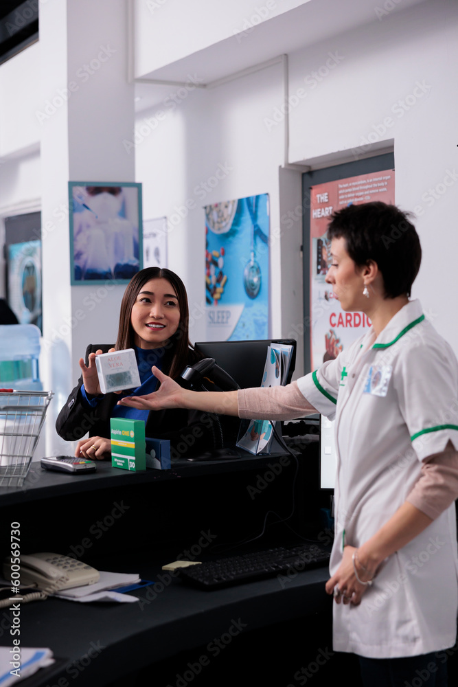 Apothecary customer asking pharmacist about vitamin at checkout, showing medical product package. Young asian woman buying food supplements and discussing medication with pharmacy cashier Apothecary customer asking pharmacist about vitamin at checkout, showing medical product package. Young asian woman buying food supplements and discussing medication with pharmacy cashier