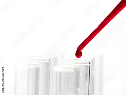 Pipette drip red liquid drops into laboratory test glass tubes. Closeup