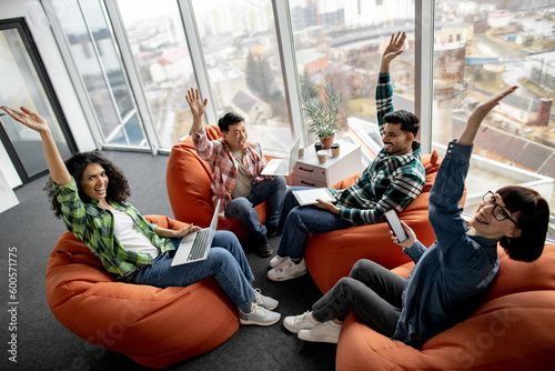 Obraz na plátně Excited male and female employees putting hands in air after stacking them while working with mobile devices in meeting space