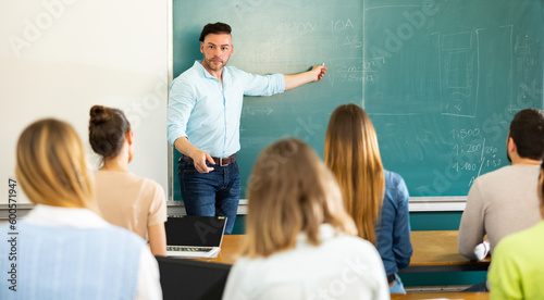 Young teacher is giving a lecture to students, standing near the blackboard in the university auditorium