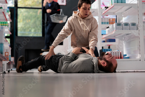 Woman helping man having foaming at mouth and convulsion during epileptic seizure in pharmacy retail store. Drugstore customer holding person having epilepsy attack, providing first aid photo