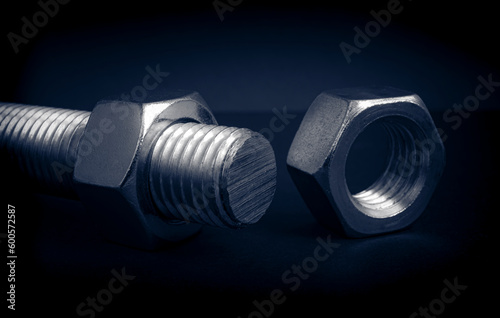Metallic nuts with threaded rod. Low-key concept picture taken in studio with soft-box and dark background representing some mechanical components.