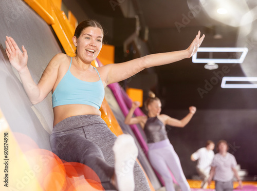 Cheerful young European female in sportswear bouncing and jumping on trampolines indoors in leisure sports center