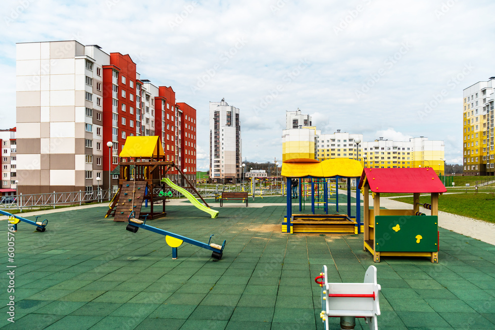 A modern outdoor playground in the courtyard of a building. Colorful children's swings and slides for recreation and games are installed. Playground on the background of residential buildings. A modern outdoor playground in the courtyard of a building. Colorful children's swings and slides for recreation and games are installed. Playground on the background of residential buildings.