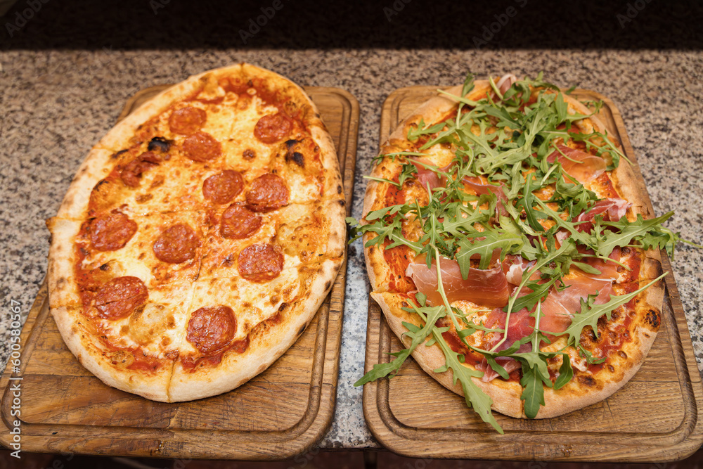Two delicious pizzas on a wooden cutting board in kitchen of pizzeria