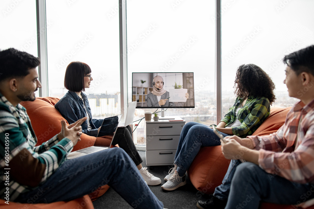 Close up of diverse professionals in coworking space participating in online briefing with colleague wearing hijab and headset. Happy entrepreneurs analyzing information received via internet service. Close up of diverse professionals in coworking space participating in online briefing with colleague wearing hijab and headset. Happy entrepreneurs analyzing information received via internet service.