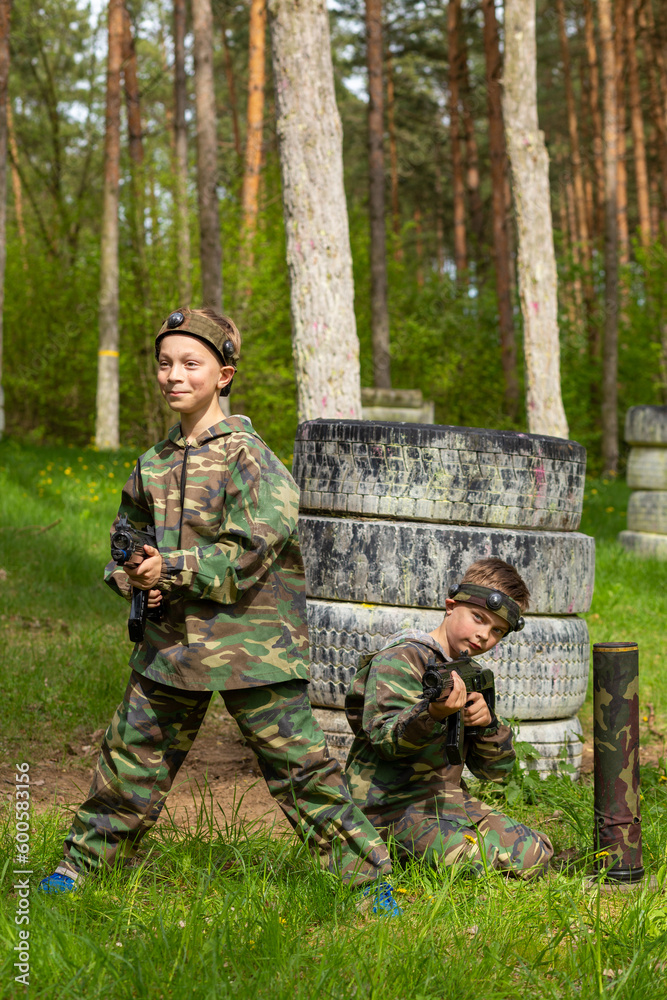 Two boys weared in camouflage playing laser tag in special forest playground.