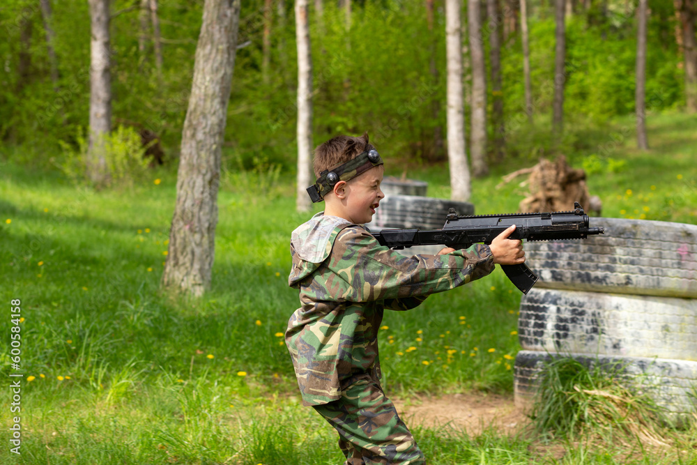 Fototapeta premium Boy weared in camouflage playing laser tag in special forest playground.