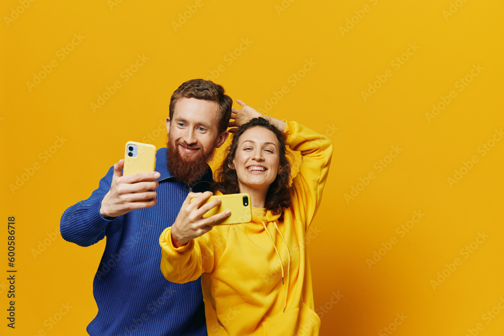 Man and woman couple smiling merrily with phone in hand social media viewing photos and videos, on yellow background, symbols signs and hand gestures, family freelancers.