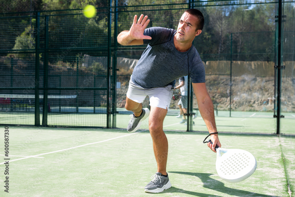 Athletic man plays padel. View through tennis net