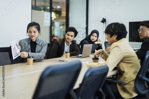 Young woman lead group of young Asian business creative team showing sales graph in brainstorm meeting presentation. 