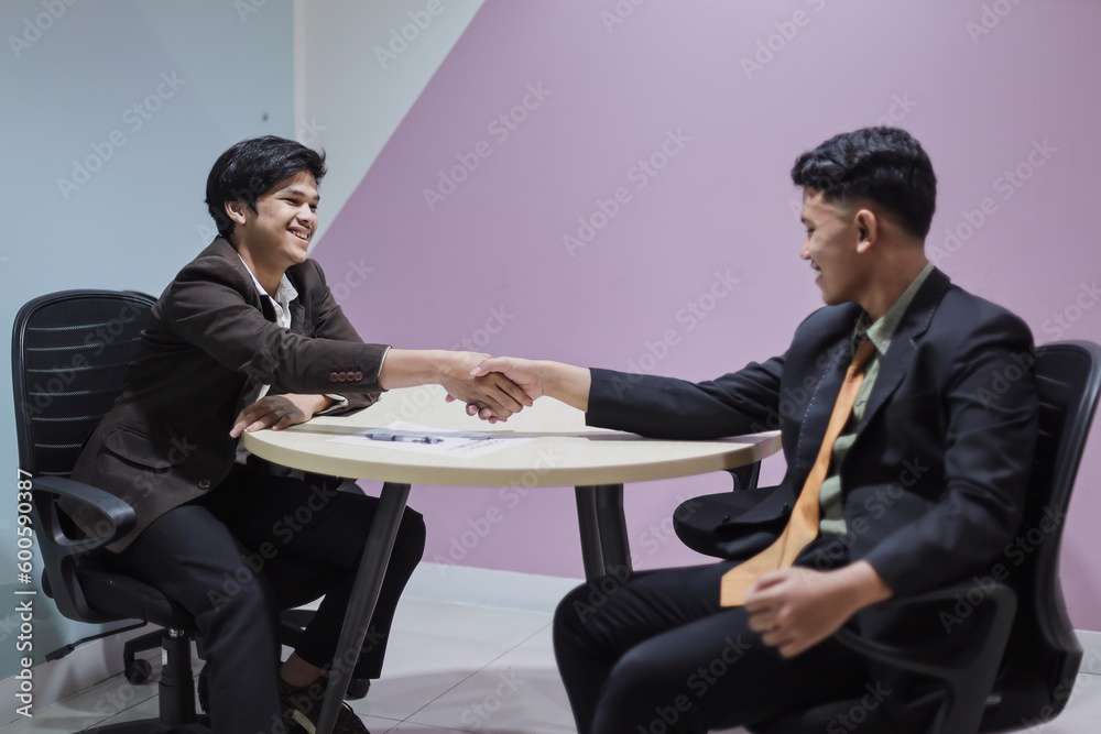 Fototapeta premium Two smiling successful young businessmen shaking hands after successful negotiations or interview in office. Business, career and placement concept. 