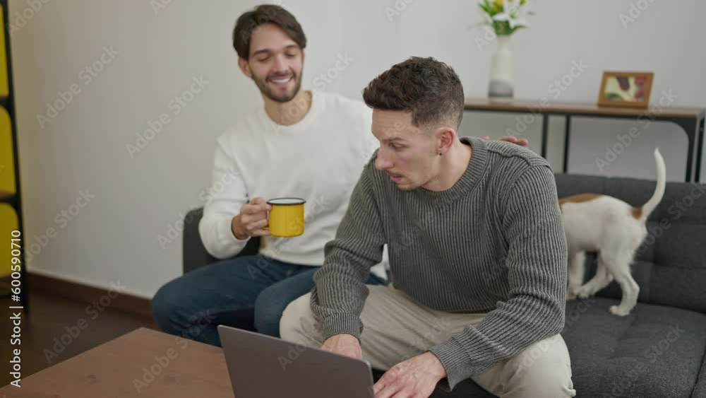 Two men couple using laptop drinking coffee kissing at home