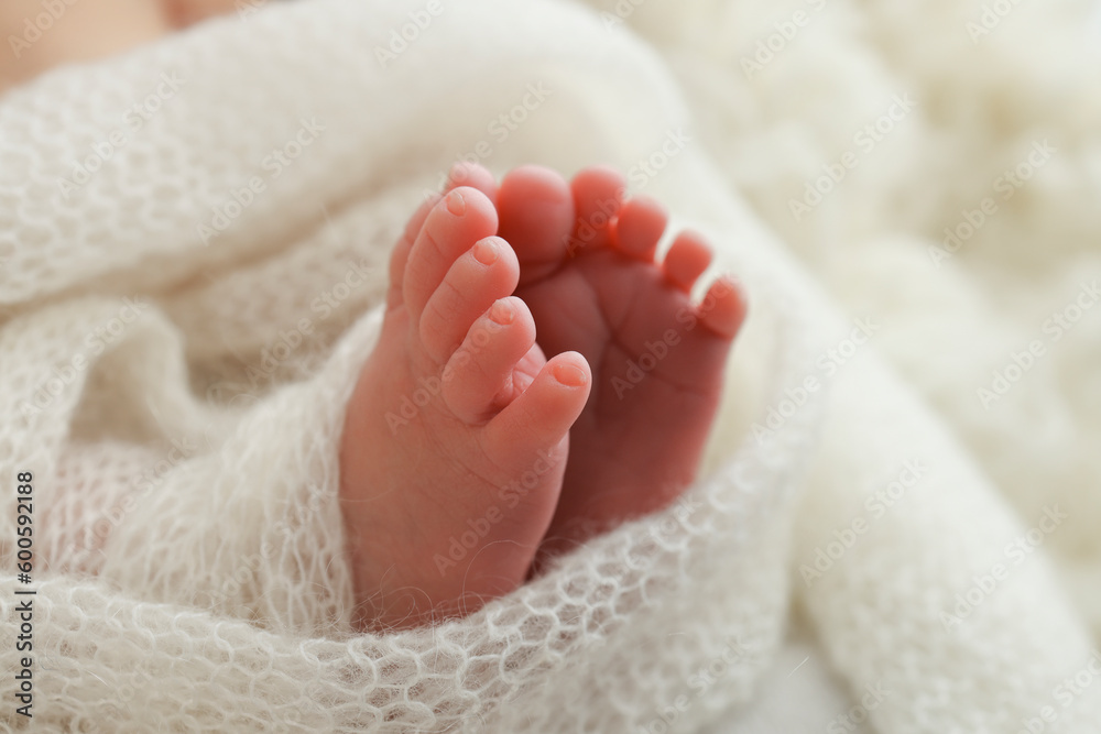 The tiny foot of a newborn baby. Soft feet of a new born in a white wool blanket. Close up of toes, heels and feet of a newborn. Knitted white heart in the legs of a baby. Macro photography The tiny foot of a newborn baby. Soft feet of a new born in a white wool blanket. Close up of toes, heels and feet of a newborn. Knitted white heart in the legs of a baby. Macro photography