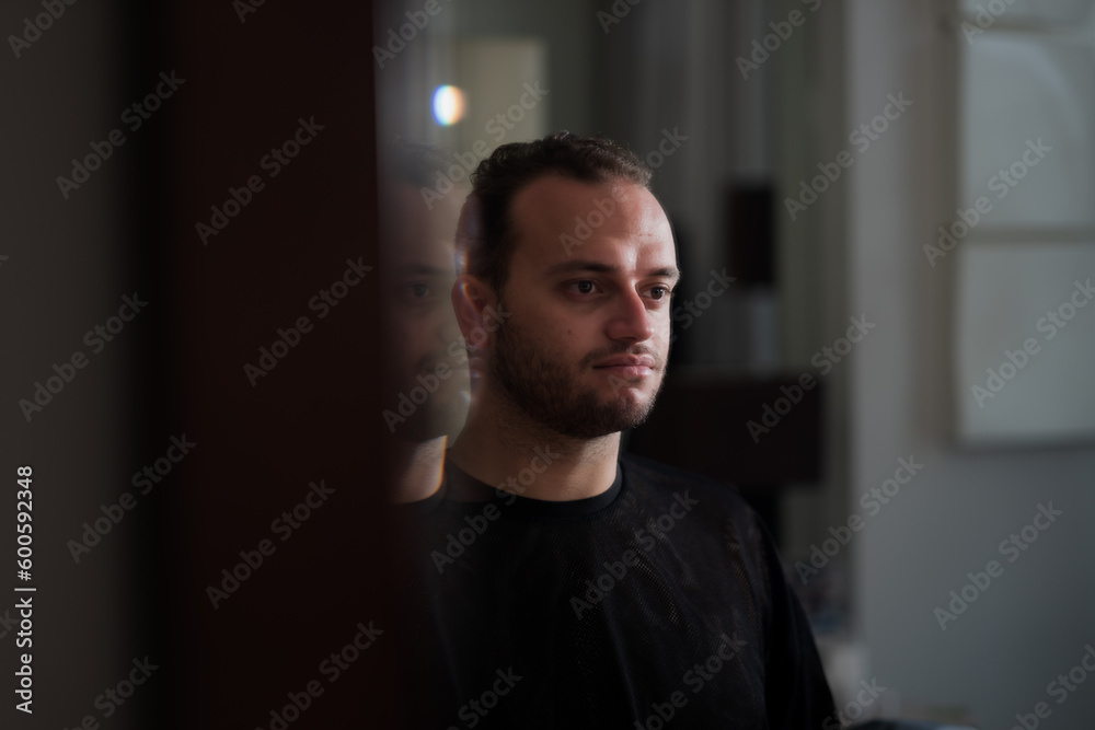 Fototapeta premium Looking at his own reflection in the mirror, a Middle Eastern man expresses a direct gaze at himself and a moment of contemplation.