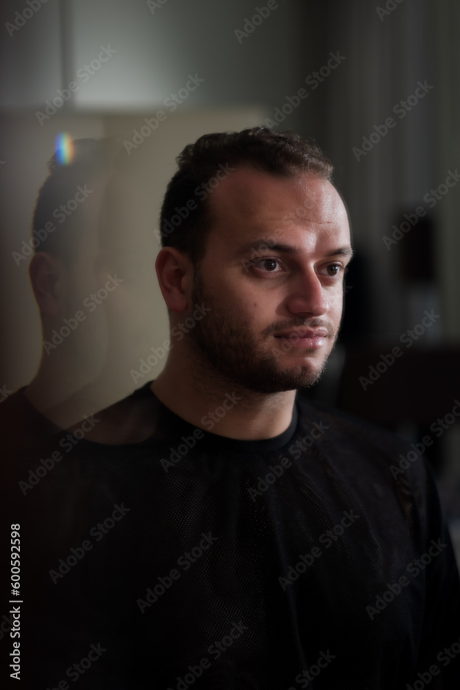 Looking at his own reflection in the mirror, a Middle Eastern man expresses a portrait with a hint of a smile and his reflection repeating behind him, suggesting optimism. Looking at his own reflection in the mirror, a Middle Eastern man expresses a portrait with a hint of a smile and his reflection repeating behind him, suggesting optimism.
