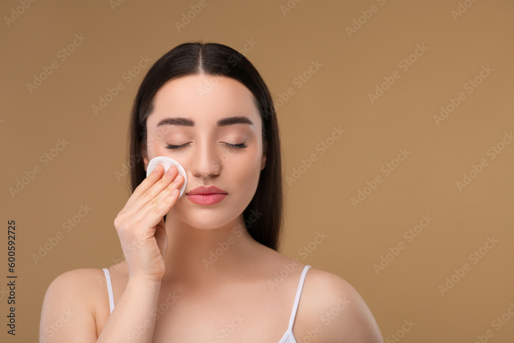 Beautiful woman removing makeup with cotton pad on beige background, space for text Beautiful woman removing makeup with cotton pad on beige background, space for text