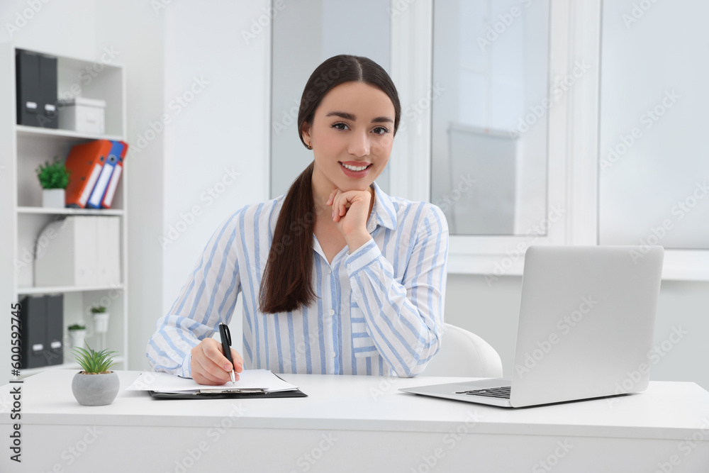 Young female intern working with laptop at table in office Young female intern working with laptop at table in office
