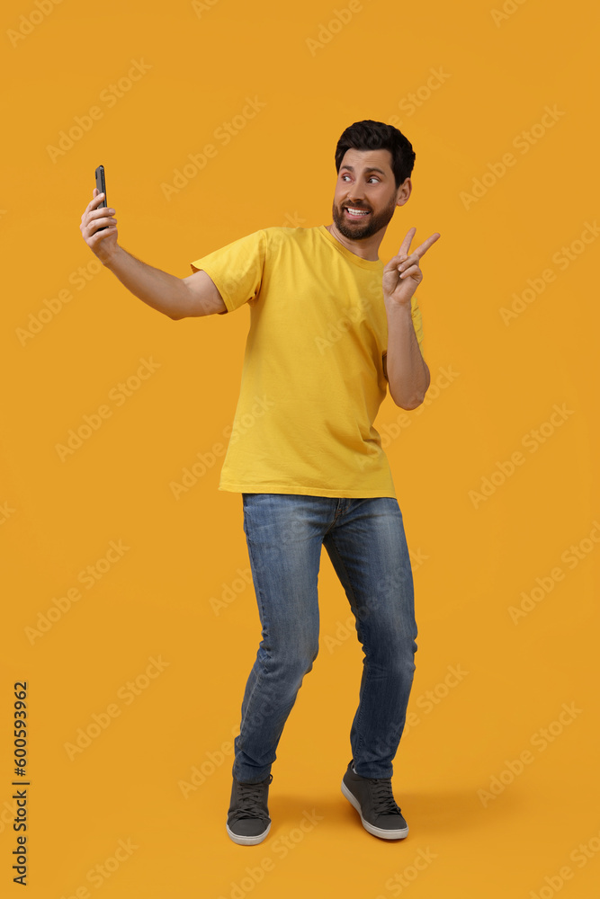 Smiling man taking selfie with smartphone and showing peace sign on yellow background Smiling man taking selfie with smartphone and showing peace sign on yellow background