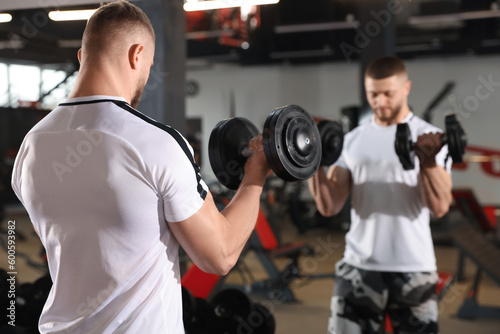Man training with dumbbells near mirror in gym