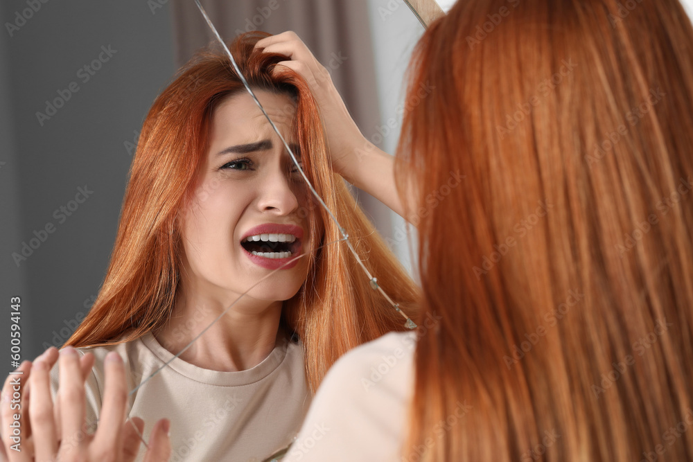 Naklejka premium Mental problems. Young woman screaming near broken mirror indoors