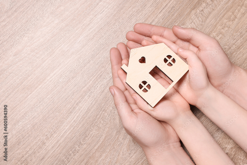 Home security concept. Man and his little child holding house model at wooden table, top view with space for text Home security concept. Man and his little child holding house model at wooden table, top view with space for text
