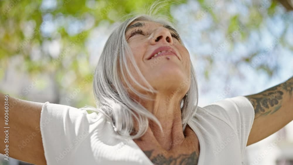 Middle age grey-haired woman breathing with arms open at park Middle age grey-haired woman breathing with arms open at park