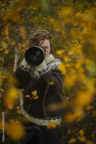 Caucasian female photographer using camera with telephoto lens in yellow autumn forest