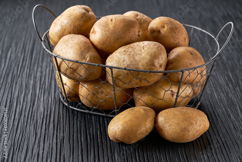 fresh raw potatoes in a metal basket on a dark woodenn table. photo