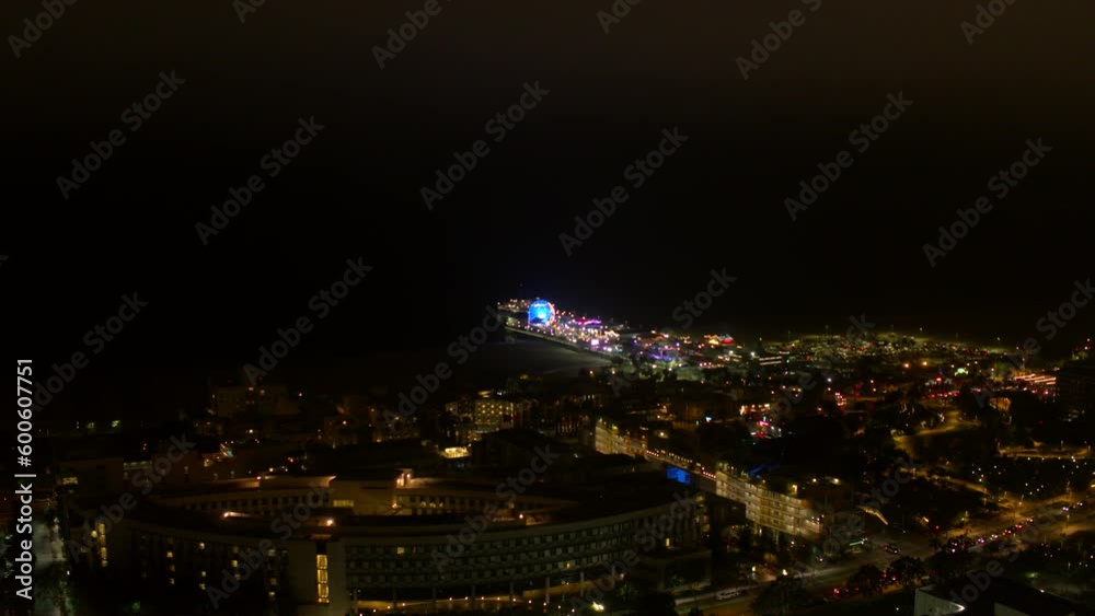 Aerial Shot Of Illuminated Buildings Near Famous Pier At Night, Drone Descending Forward Towards Santa Monica Pier - Los Angeles, California Aerial Shot Of Illuminated Buildings Near Famous Pier At Night, Drone Descending Forward Towards Santa Monica Pier - Los Angeles, California