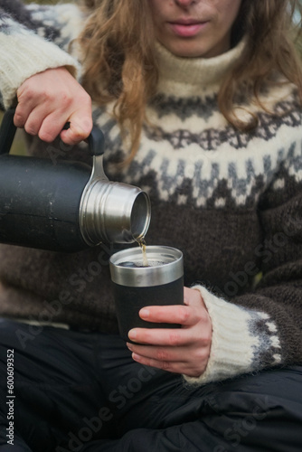 Woman pouring a tea from thermos outdoors