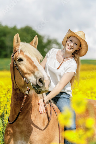 Portrait of a female equestrian riding her haflinger horse in spring outdoors in front of a rural countryside landscape with blooming yellow flowers