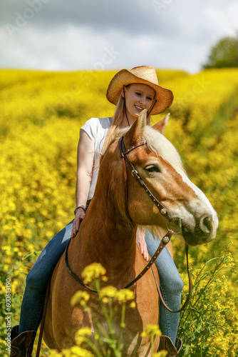 Portrait of a female equestrian riding her haflinger horse in spring outdoors in front of a rural countryside landscape with blooming yellow flowers