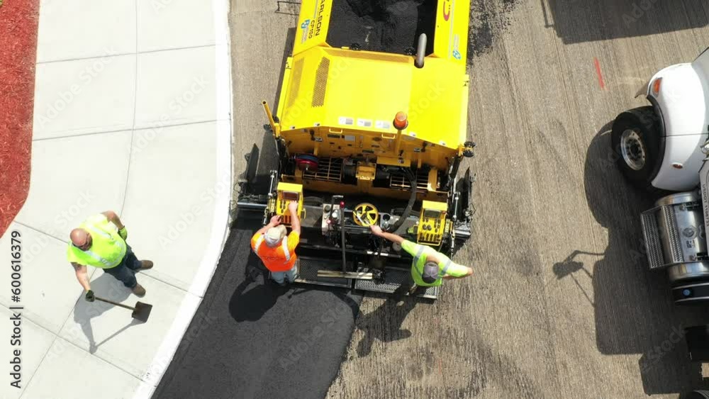 Aerial top down, construction workers operate asphalt paver to pave new road