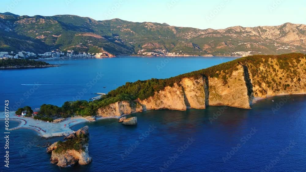 Island of St. Nicholas with vegetation on shores in the Adriatic Sea against the backdrop of coastal towns, the Montenegrin mountains and clear sky Island of St. Nicholas with vegetation on shores in the Adriatic Sea against the backdrop of coastal towns, the Montenegrin mountains and clear sky