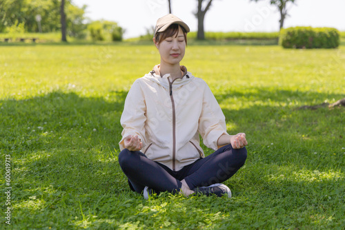 公園の木陰で瞑想ヨガをする女性