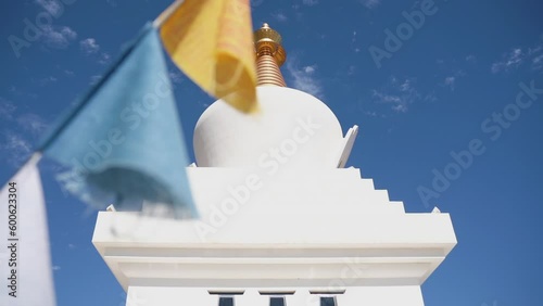 white golden stupa with colourful prayer flag against blue clear sky in slow motion 