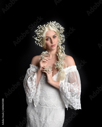 Close up portrait of beautiful women with long blonde hair, wearing white fantasy princess ball gown, holding pretty baby breath flowers, isolated on black studio background 