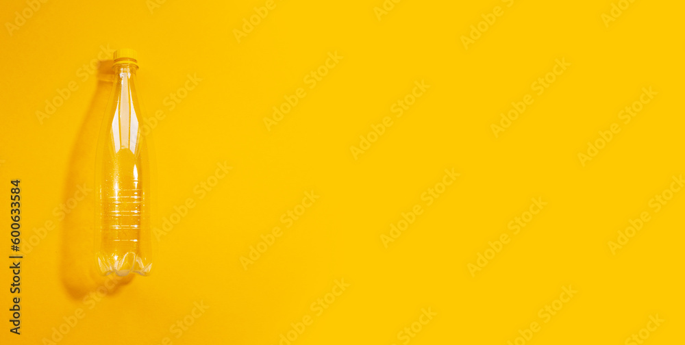 Close-up top view of empty transparent plastic bottle on yellow background with copy space. Panoramic banner view. Close-up top view of empty transparent plastic bottle on yellow background with copy space. Panoramic banner view.