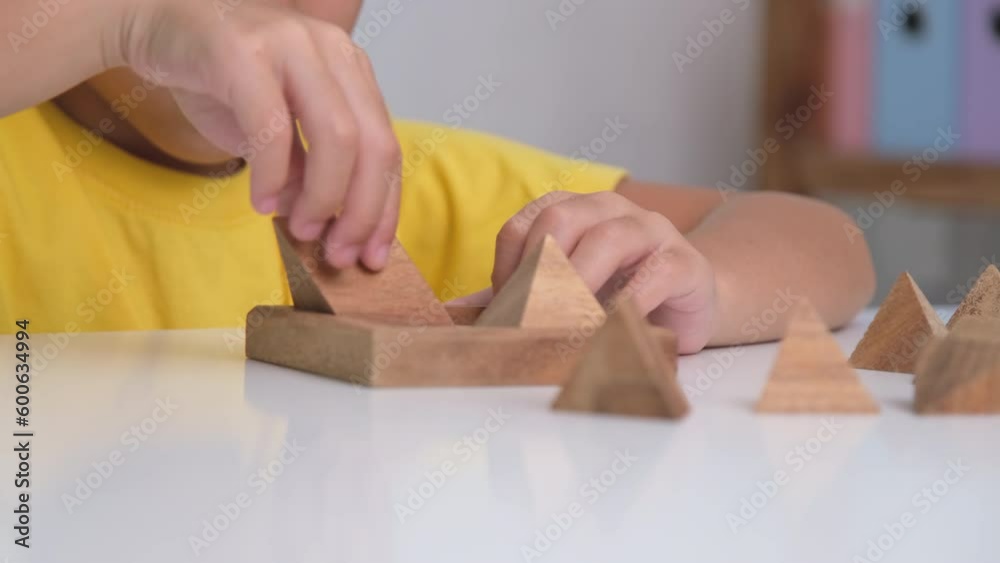 Asian cute little girl playing with wooden toy jigsaw puzzle pyramid on table. Healthy children training memory and thinking. Wooden puzzles are games that increase intelligence for children.