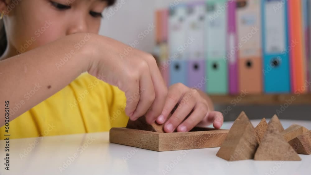 Asian cute little girl playing with wooden toy jigsaw puzzle pyramid on table. Healthy children training memory and thinking. Wooden puzzles are games that increase intelligence for children. Asian cute little girl playing with wooden toy jigsaw puzzle pyramid on table. Healthy children training memory and thinking. Wooden puzzles are games that increase intelligence for children.