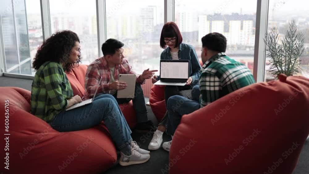 Joyful caucasian female holding laptop while multicultural team members with gadgets talking in workplace interior. Busy architects outlining details of construction blueprints via mobile devices. Joyful caucasian female holding laptop while multicultural team members with gadgets talking in workplace interior. Busy architects outlining details of construction blueprints via mobile devices.