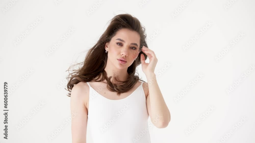 Attractive beautiful young woman touching curly hair looking at camera playfully posing while standing against white studio background. Cosmetics for hairstyles and hair care concept Attractive beautiful young woman touching curly hair looking at camera playfully posing while standing against white studio background. Cosmetics for hairstyles and hair care concept