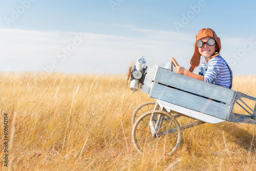 Little boy is playing the plane.
Happy and funy child imagines himself an aircraft pilot and plays in a aviator costume in an open-air field against a blue sky on a summer sunny day. 