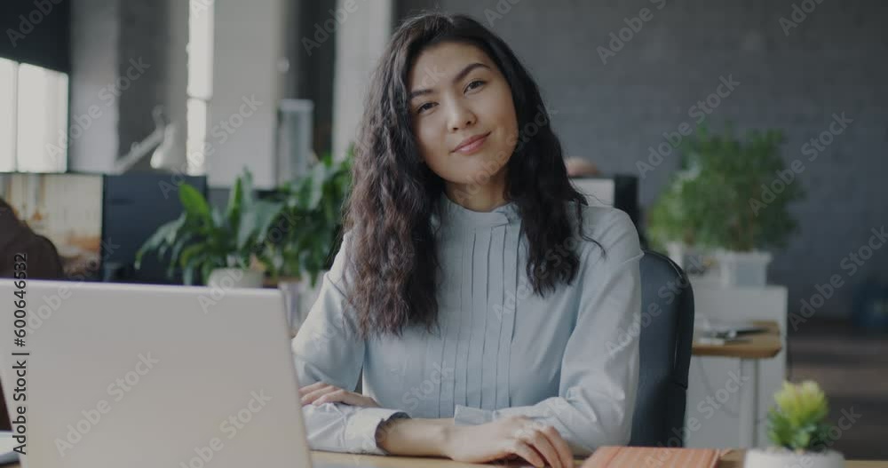 Slow motion portrait of joyful Asian businesswoman smiling looking at camera in shared office. Employment and successful career concept. Slow motion portrait of joyful Asian businesswoman smiling looking at camera in shared office. Employment and successful career concept.
