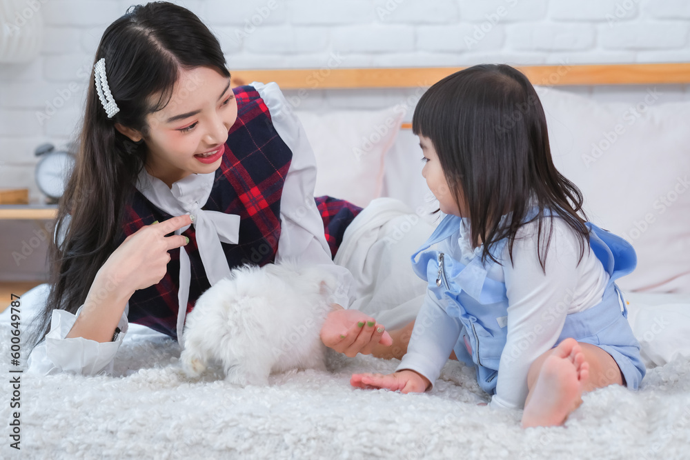 Beautiful asian girl and little girl playing with little white dog with smile on bed in bedroom. Beautiful asian girl and little girl playing with little white dog with smile on bed in bedroom.