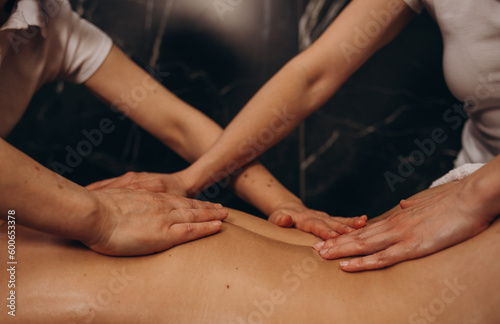 Two massaging therapist makes massage back for woman. Massage in four hands in SPA salon. Sensual healthy massaging in 4 hands of professional masseur. Concept of health care and female beauty.