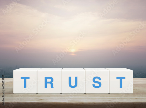 Trust letter on white block cubes on wooden table over modern city tower and skyscraper at sunset, vintage style, Building trust business concept