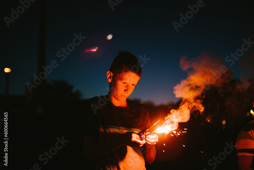 Boy holds a fire sparkler on July 4th in the dark night photo